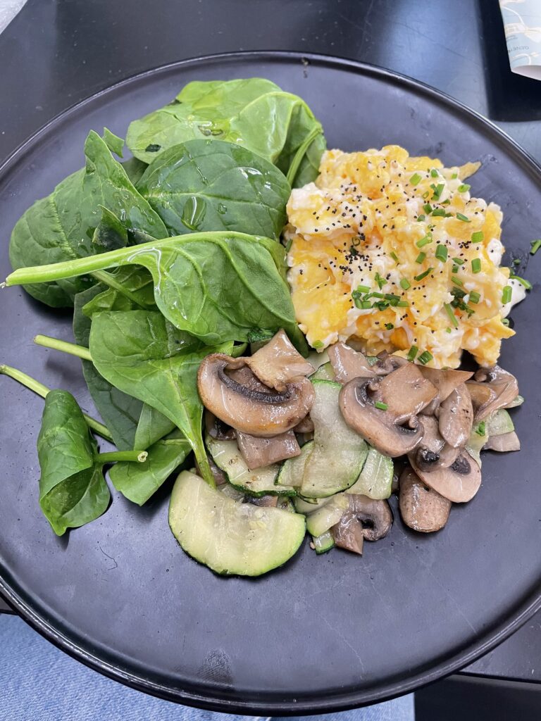 Dark plate of scrambled eggs and herbs, fresh spinach, and cooked mushrooms and zucchinni.