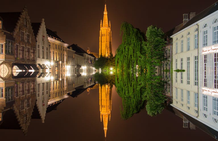 Stunning view of Bruges with illuminated reflections on the water at night, showcasing historic architecture.