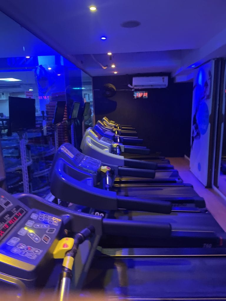6 treadmills in a gym with air conditioner unit on wall and dim blue lighting