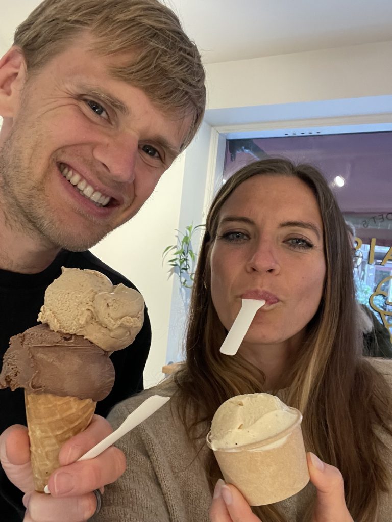 Man with double scoop ice cream cone next to woman with spoon in mouth and single scoop ice cream.