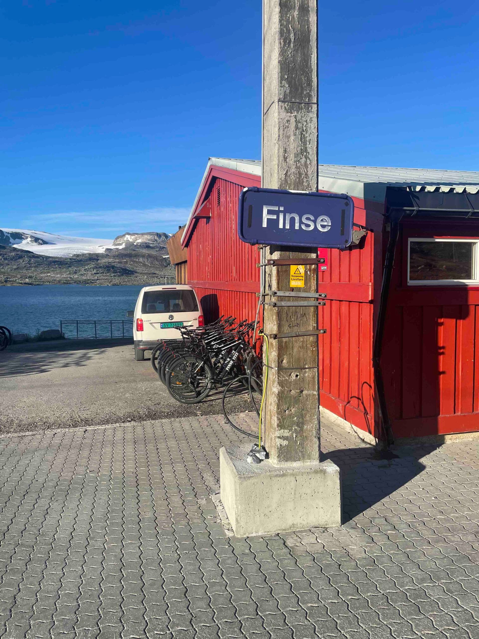Town sign on wooden pole in front of red barn and fjord