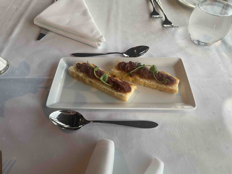 Olive and tomato tapenade on white bread on white table cloth with 2 spoons